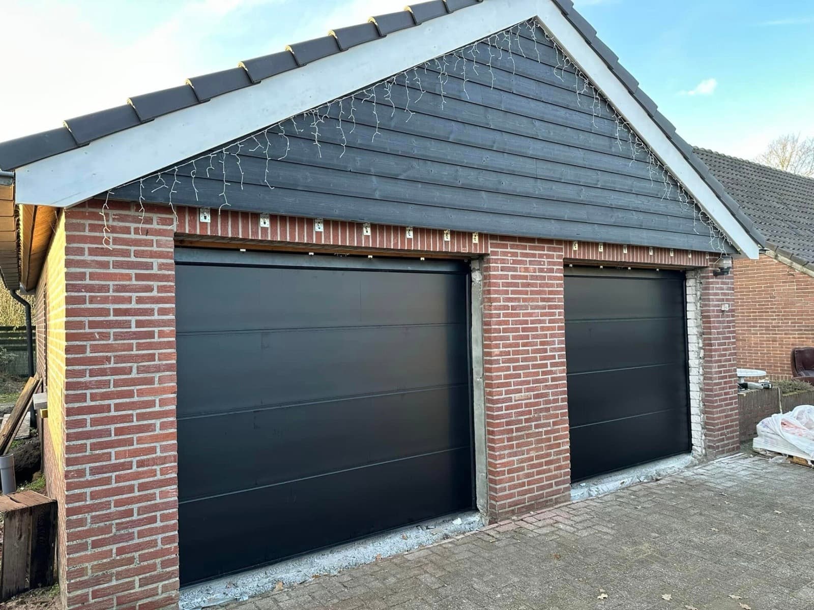 Twee antraciet sectionaaldeuren in een bakstenen garage