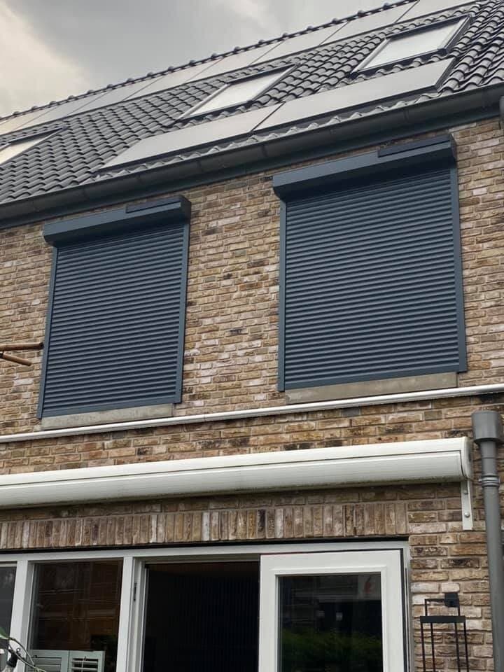 Antraciet rolluiken voor de ramen van een bakstenen woning