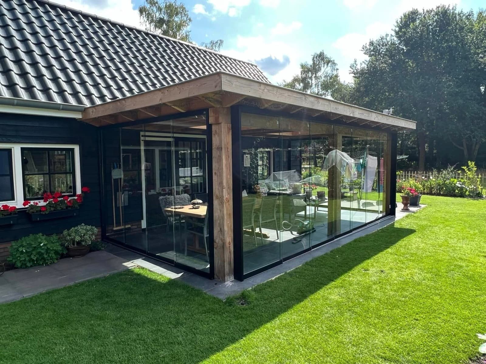 Overkapping van douglashout met glazen schuifwanden tegen een donker houten huis